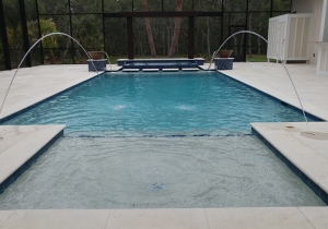 Geometric concrete pool with deck jets and travertine deck